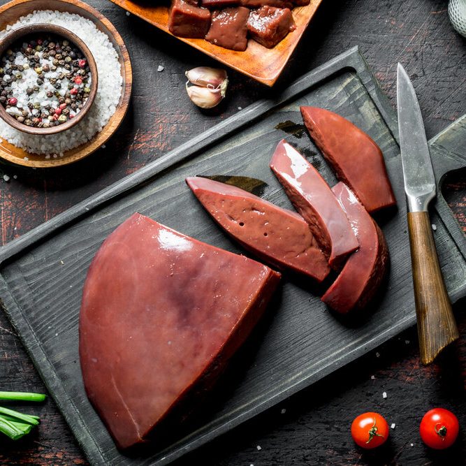 Sliced raw liver with tomatoes, herbs and spices. On dark rustic background