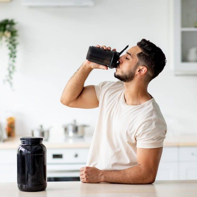 Young,Arab,Guy,Drinking,Protein,Shake,From,Bottle,At,Kitchen,